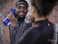 Smiling athletic man and woman with water bottles at wall