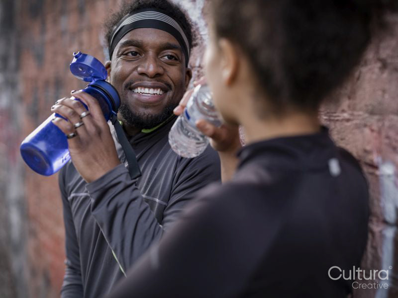 Smiling athletic man and woman with water bottles at wall