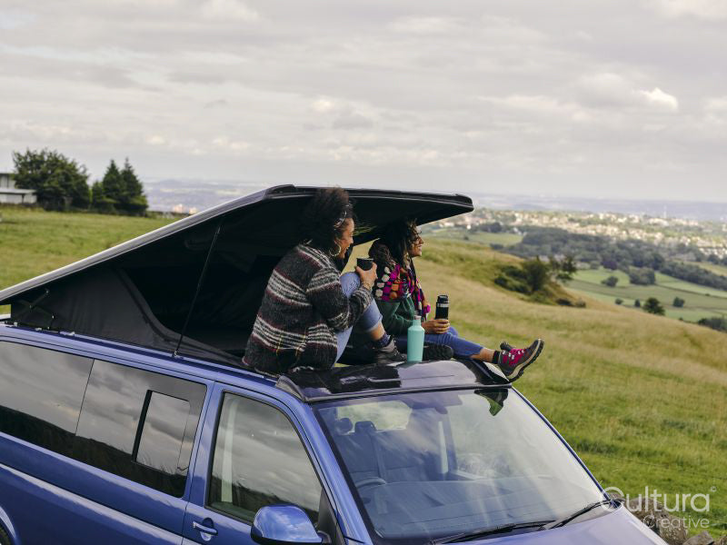Women sitting on roof of van and looking at landscape