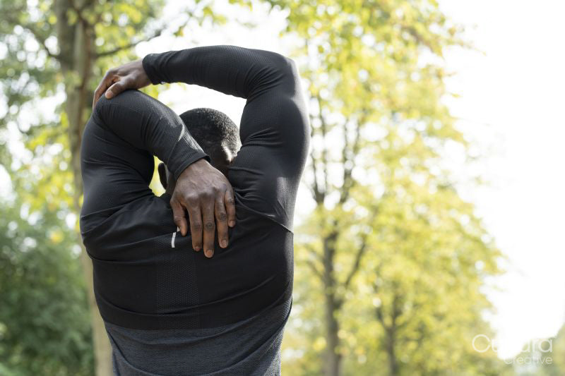 Rear view of athletic man stretching arm in park