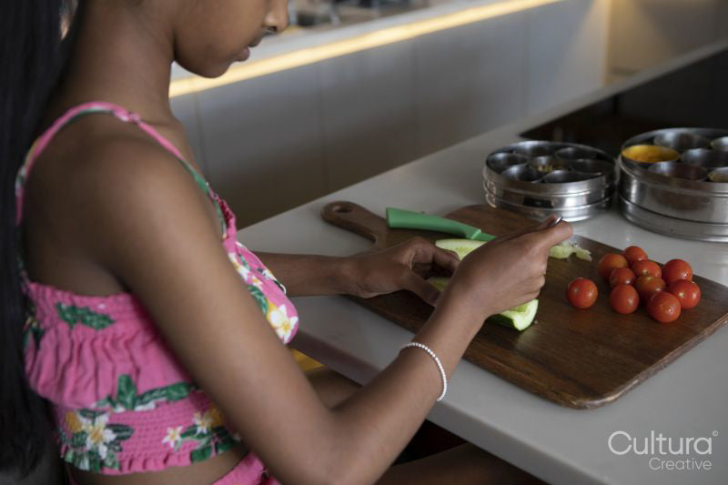 Close-up of girl cutting cucumber in kitchen