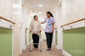Nurse helping senior lady to walk with mobility walker at nursing home
