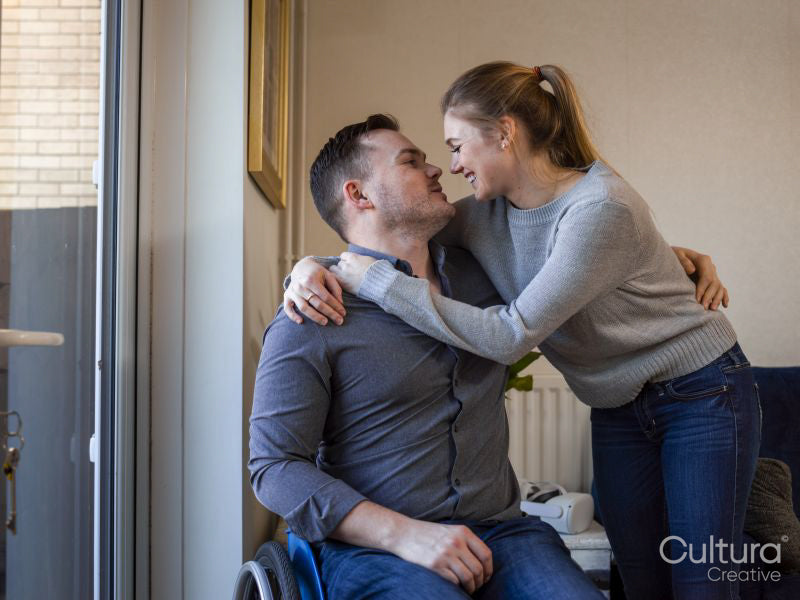 Woman embracing man on wheelchair at home
