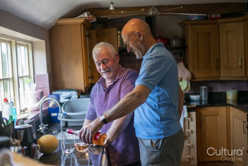 Senior male couple pouring drinks in kitchen