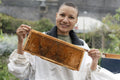 Portrait of smiling female beekeeper holding frame from beehive in urban garden