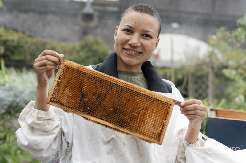 Portrait of smiling female beekeeper holding frame from beehive in urban garden