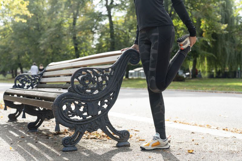 Low section of woman stretching leg at bench in park