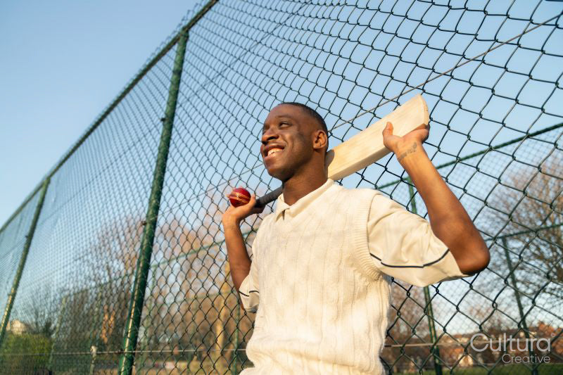 Portrait of smiling cricketer leaning on fence on outdoors sports court