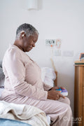 Senior woman in pajamas sitting on bed, holding pill organizer