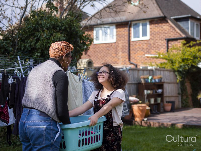 Mother with daughter carrying laundry basket across backyard
