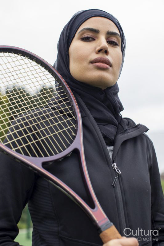Portrait of woman in black sports clothing and hijab holding tennis racket