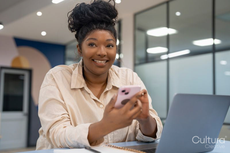 Businesswoman using phone and laptop in office