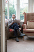 Senior man sitting in armchair and reading newspaper in nursing home