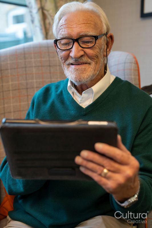 Senior man sitting in armchair and using tablet in nursing home