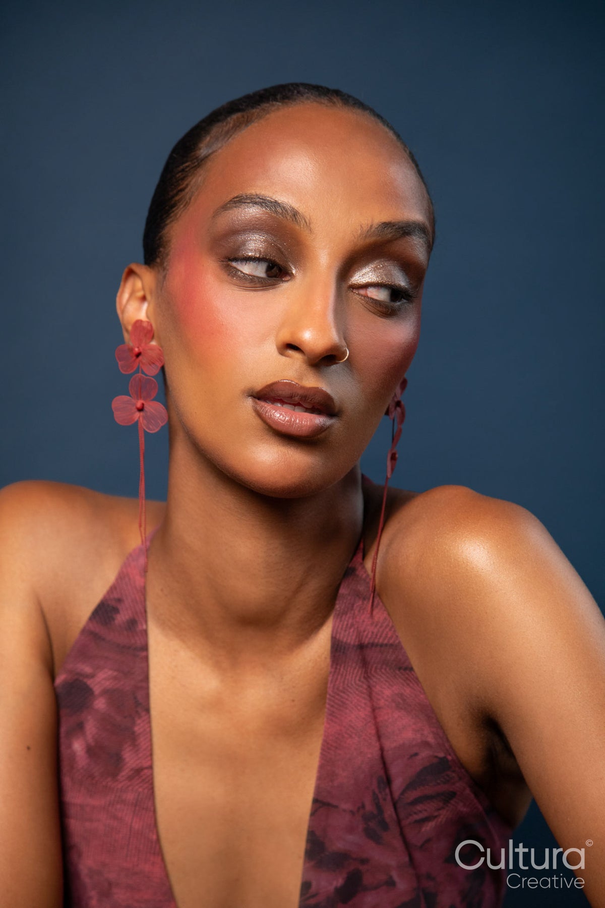 Woman in a burgundy dress with red earrings on a blue background