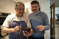 Smiling father and adult son looking at smart phone in kitchen