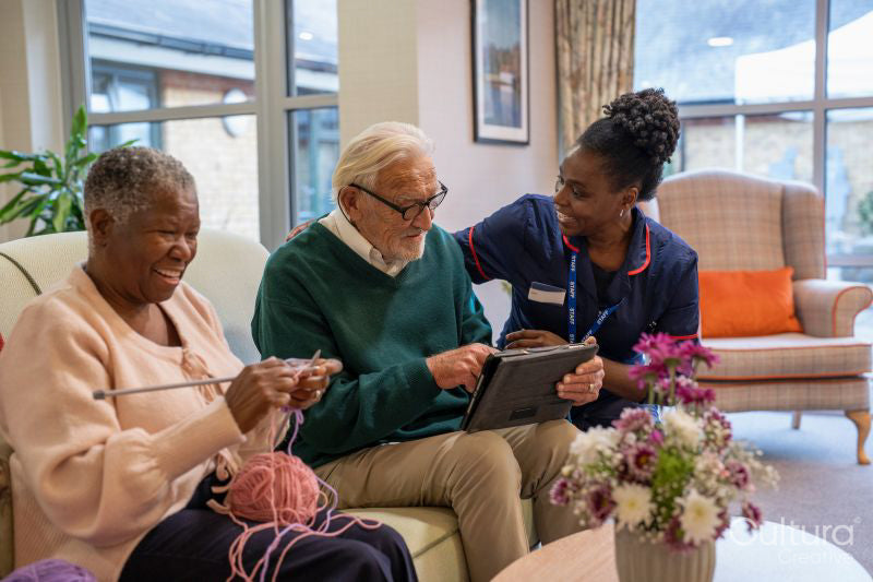 Smiling nurse helping senior man use tablet in nursing home