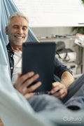 Smiling mature man lying in hammock and using digital tablet