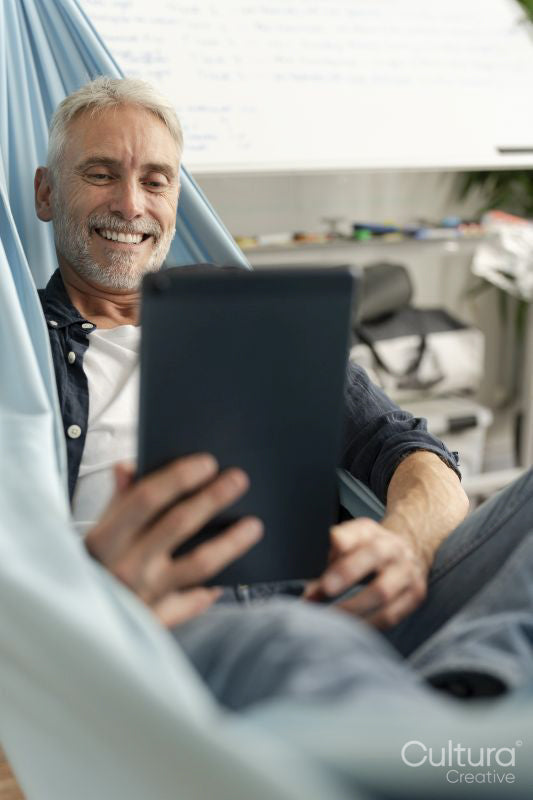 Smiling mature man lying in hammock and using digital tablet