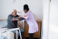 Caregiver helping senior man to get up from bed