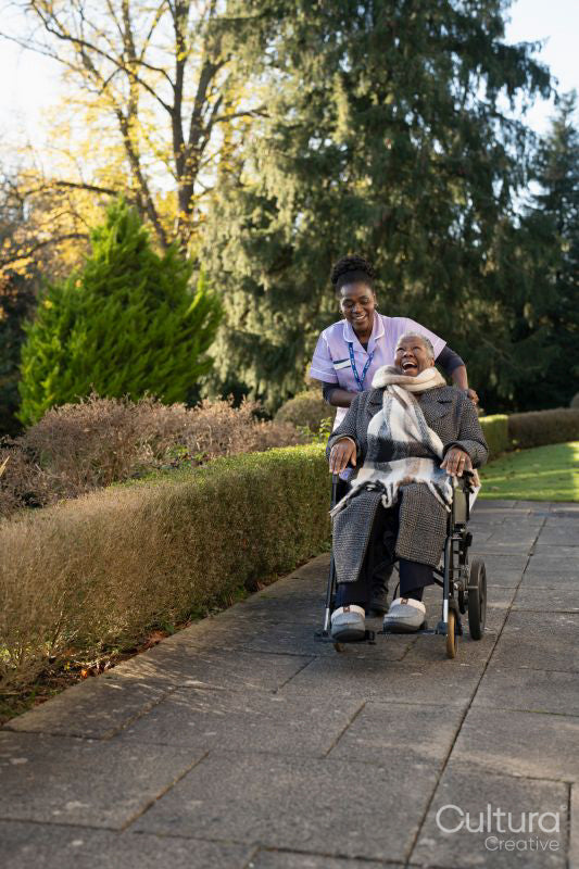 Nurse and senior woman in wheelchair going on walk in park
