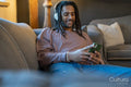 Man with dreads using phone and listening to music while relaxing on sofa