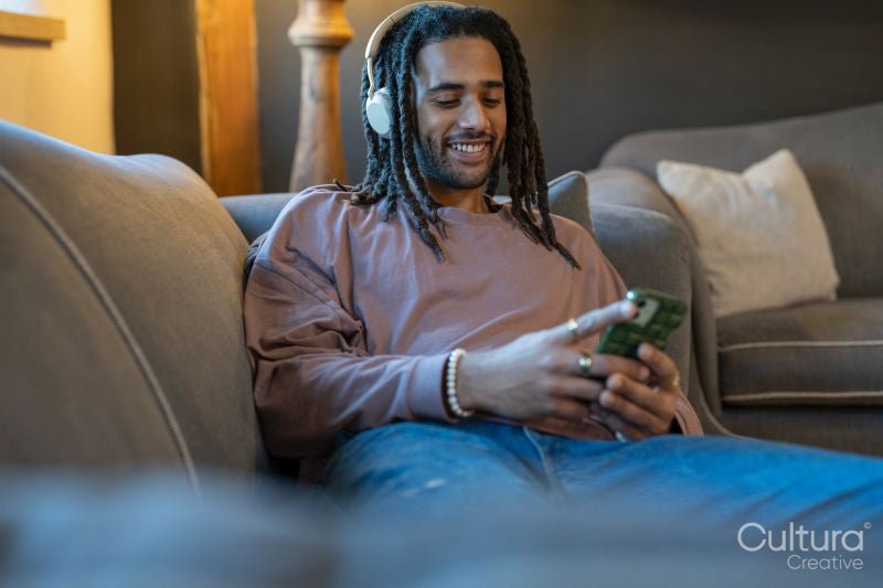 Man with dreads using phone and listening to music while relaxing on sofa