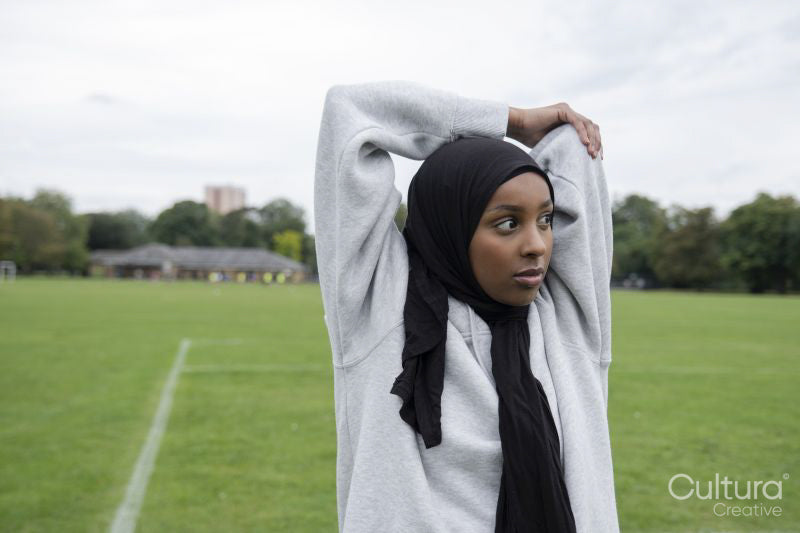 Portrait of woman in hijab stretching arm in soccer field