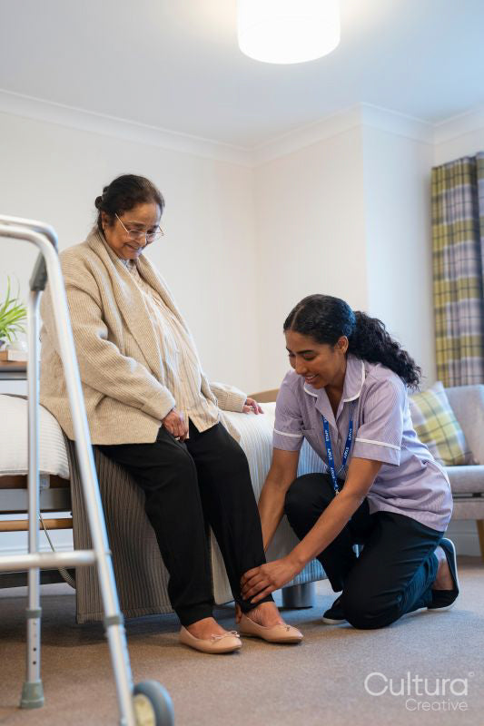 Nurse helping senior lady to put on her shoes at nursing home