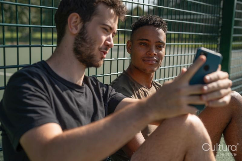 Two men looking at smart phone in tennis court