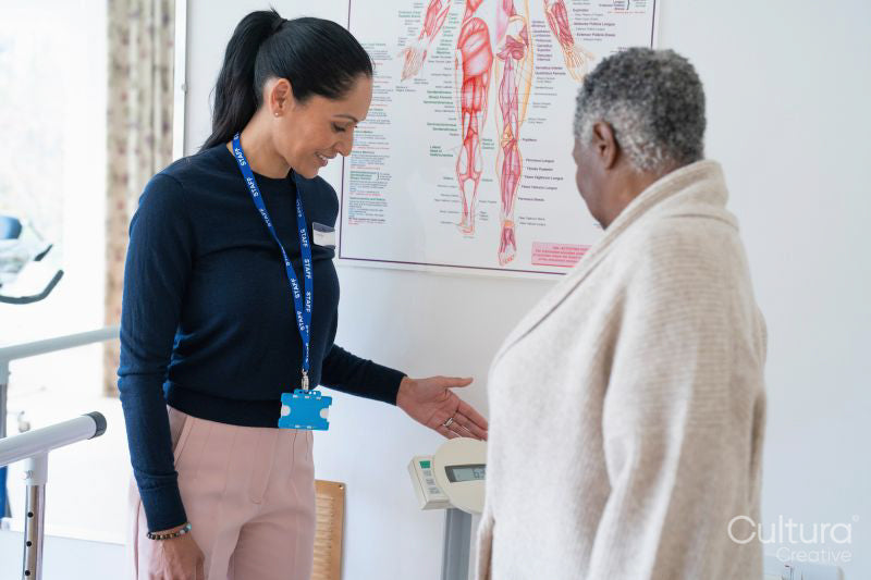 Smiling female therapist assisting senior woman standing on weight scale