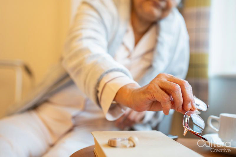 Senior lady taking eyeglasses from table while sitting in chair at nursing home