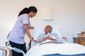 Nurse helping with remote control to senior man lying in adjustable bed in room at nursing home
