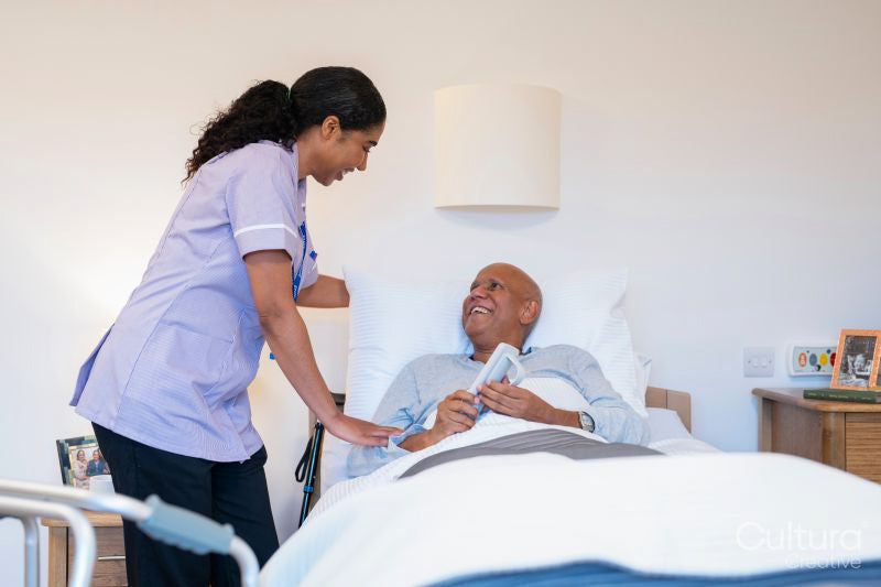 Nurse helping with remote control to senior man lying in adjustable bed in room at nursing home