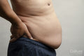 Profile view of man with pot belly against gray background