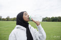 Portrait of woman in hijab drinking water from bottle in soccer field