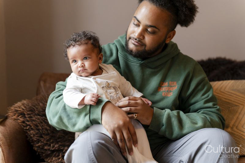 Baby daughter sitting on fathers lap at home